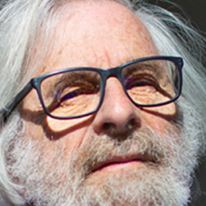 Outdoor photo of Leslie Lamport wearing a blue shirt with his hand up to his shoulder